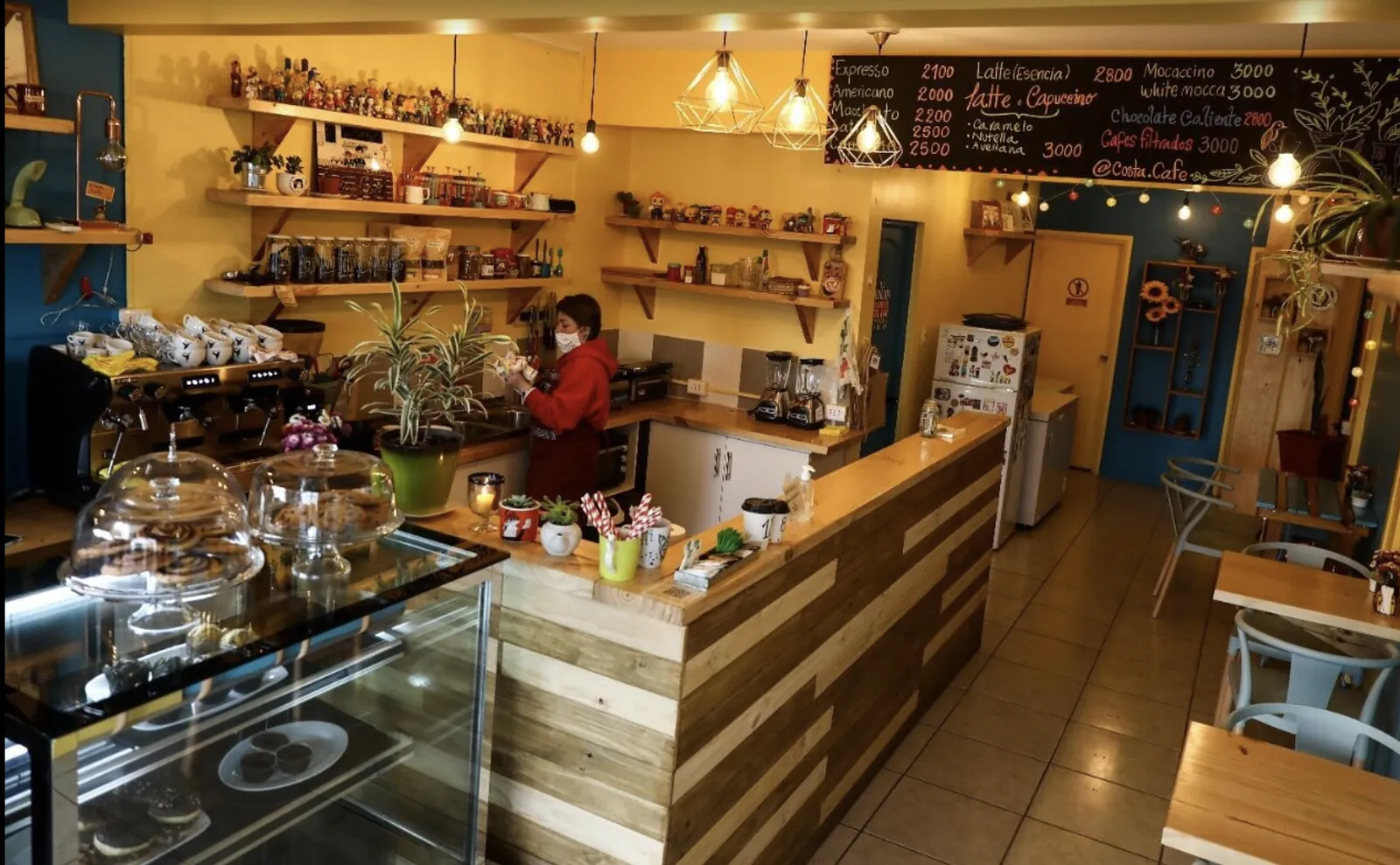 Interior de Costa Café en Algarrobo: barra de madera, vitrina de pastelería y pizarra de cafés